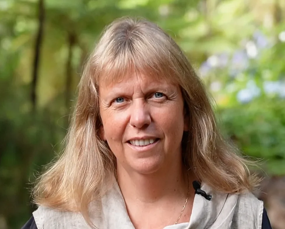 Dr. Inken Barth, Porträt einer lächelnden Frau mit blonden, schulterlangen Haaren in einer grünen Umgebung.