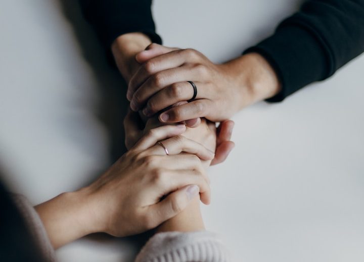 Hände unterschiedlichen Hautfarbens liegen übereinander auf einem Tisch.