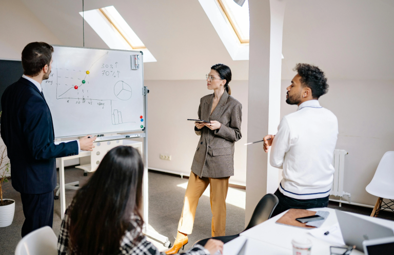 Personen besprechen ein Projekt vor einem Whiteboard in einem modernen Büro.